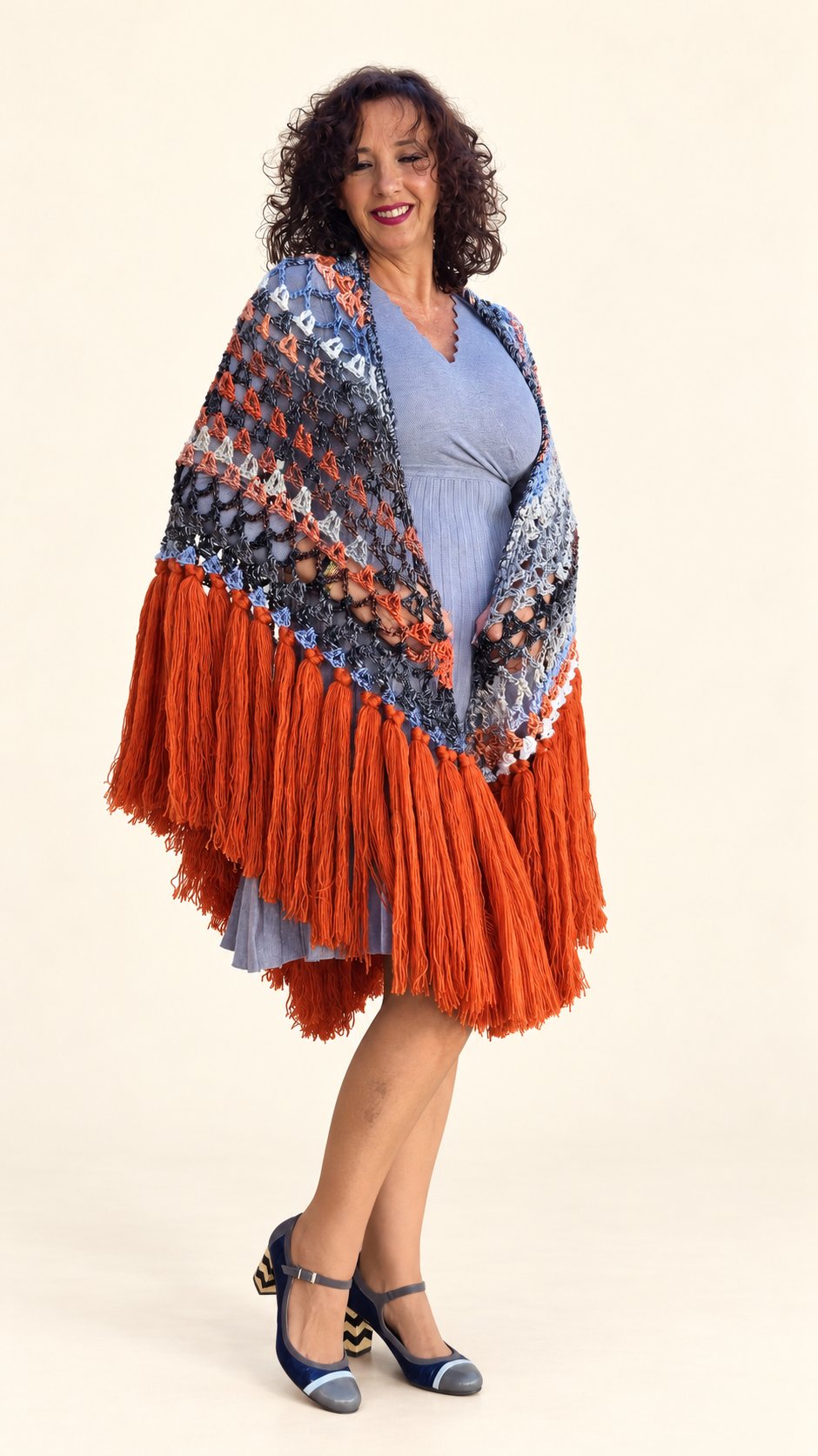 Chal Conchi de lana multicolor con flecos naranja caldera, abierto sobre los hombros sobre fondo crema