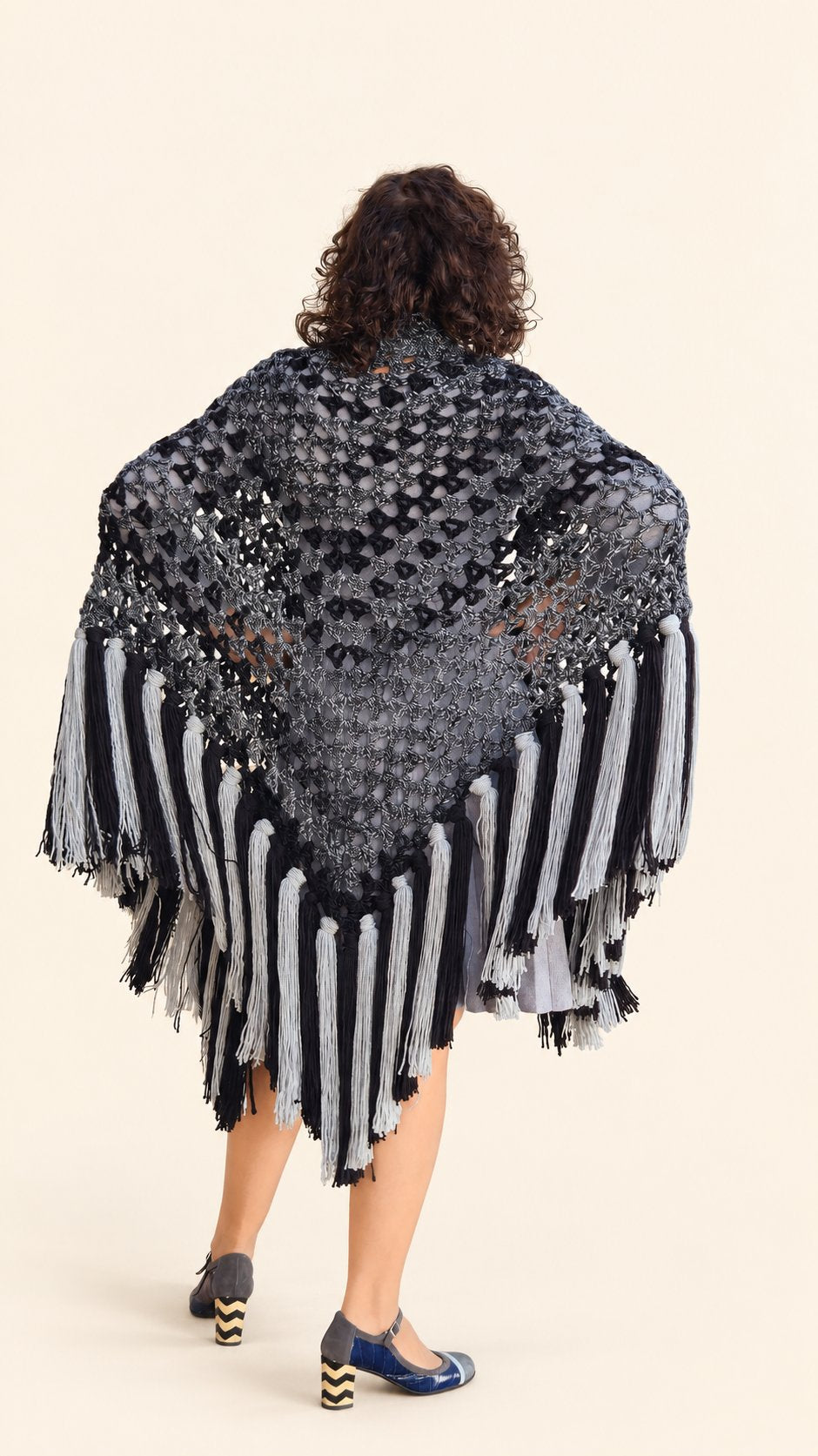 Chal Marian de lana gris y negra con flecos grises y negros, espalda con brazos abiertos, fondo crema