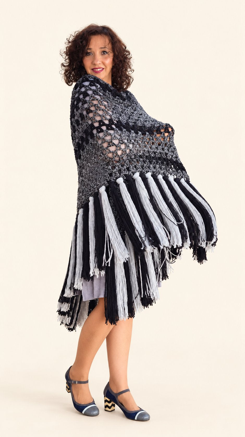 Chal Marian de lana gris y negra con flecos grises y negros, vista lateral con flecos en movimiento, fondo crema